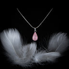 Necklace with a pink teardrop pendant on a black background with white feathers.
